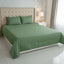 Green bedspread on a bed in a bedroom with a lamp and headboard.