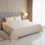 Neatly made bed with beige bedding in a well-lit bedroom.