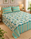 A floral and striped bedding set on a bed in a styled bedroom, featuring a cream background with blue and green floral print and matching striped pillows and bed skirt.