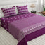 A purple and white patterned bedspread set with matching pillowcases on a bed in a bright bedroom setting.