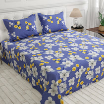 A bed dressed in a blue floral print bedding set, featuring a duvet cover and two matching pillowcases with large white and yellow flowers, shown in a bright bedroom setting.