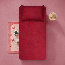 Red patterned bedspread on a pink background with decorative items.