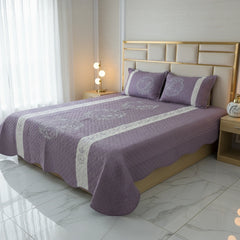 Bed with purple bedding and pillows in a well-lit room