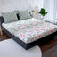 Floral patterned bedspread on a bed in a bedroom setting with pillows and a nightstand.