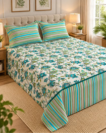 A floral and striped bedding set on a bed in a styled bedroom, featuring a cream background with blue and green floral print and matching striped pillows and bed skirt.