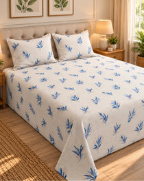 A neatly made bed in a warm, styled bedroom setting, featuring a white bedspread and matching pillowcases with a blue leaf pattern.