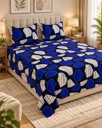 A bed dressed in a blue and white geometric patterned bedspread and matching pillowcases, styled in a warm, modern bedroom setting with bedside tables, lamps, and a rug.