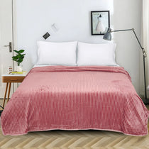 A pink ribbed fleece blanket is draped over a bed with two white pillows in a bright, modern bedroom setting.